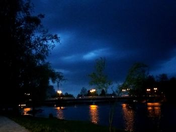 Illuminated city by river against sky at night