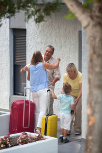 Mature couple greeting grandson with daughter at entrance of house