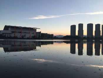 Buildings by lake against sky during sunset in city