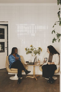 Happy female colleagues discussing while sitting on chairs at office