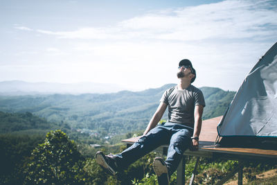 Young man sitting on mountain against sky