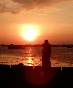 Rear view of man photographing sea against sunset sky