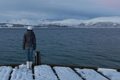 Rear view of woman standing on jetty against sky during winter