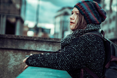 Woman in warm clothing standing by retaining wall in city