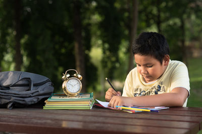 Boy studying at table against trees
