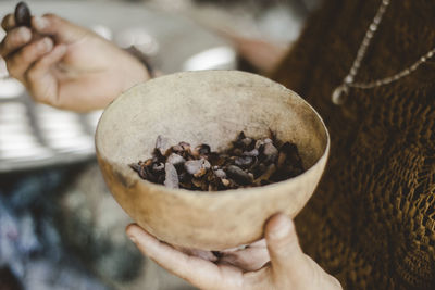 Close-up of hand holding a bowl with cocoa nibs