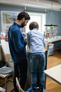 Rear view of teacher assisting male student in making project at school