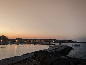 Sea by buildings against sky during sunset