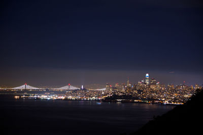 Illuminated city by sea against sky at night
