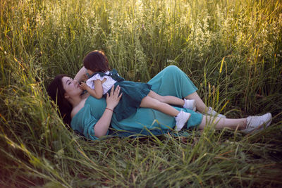 Koreans family mother and daughter in green dresses lie in the long grass on the field at sunset