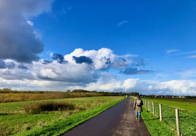 Rear view of woman walking on a rural road under a blue sky with white and grey clouds