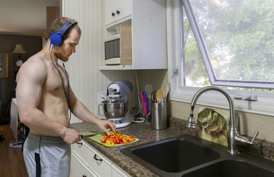Side view of shirtless young man chopping food on kitchen counter at home