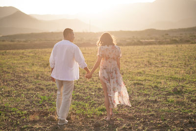 Rear view of couple holding hands white walking on field