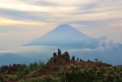 Group of people on mountain against cloudy sky