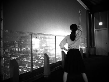 Rear view of woman with arm raised standing at balcony