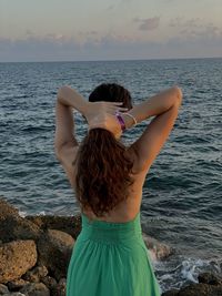 Rear view of woman with long hair standing at beach against sky