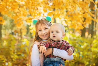 Portrait of smiling girl with brother against maple leaves