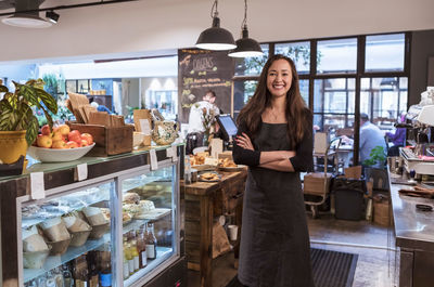 Portrait of smiling saleswoman with arms crossed by retail display at cafe