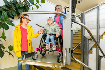 Mother and child living with cerebral palsy using wheelchair lift to access public building.