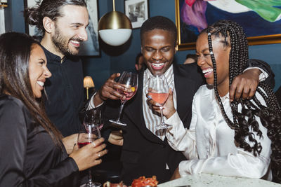 Cheerful female and male friends with wineglasses celebrating during party in bar