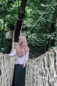 Woman wearing hijab standing on footbridge in forest