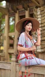 Portrait of young woman wearing hat standing by railing