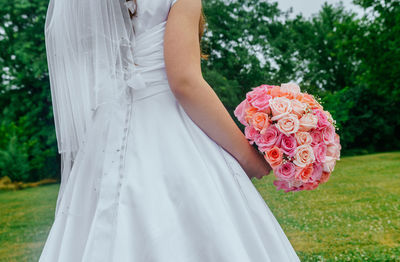 Midsection of bride holding bouquet in back yard