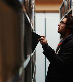 Side view of young man looking at books in library