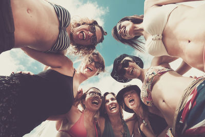 Low angle view of cheerful friends standing against sky