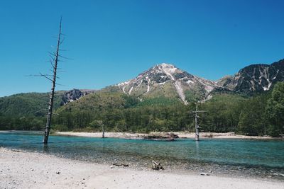 Scenic view of beach and mountains against clear blue sky