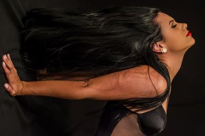Midsection of woman with arms raised against black background