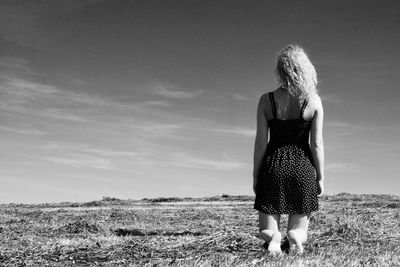 Rear view of woman kneeling on field against sky