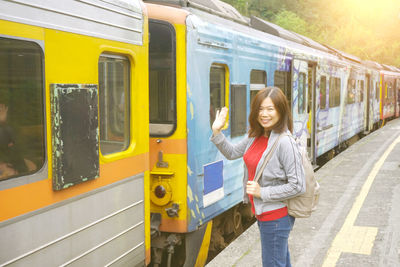 Portrait of smiling woman waving hand while standing by train