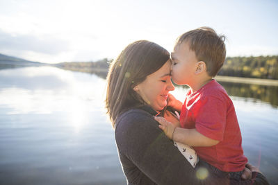 Son kissing mother on forehead against lake