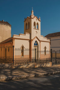 Facade of small church and belfry behind iron fence, in a sunny day at são manuel, brazil.