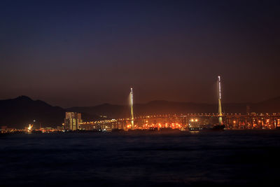 Illuminated city by sea against sky at night