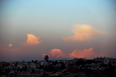 Cityscape by snowcapped mountain against sky during sunset