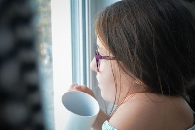 Side view of cute girl holding mug by window at home