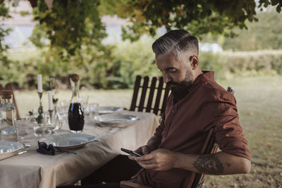 Midsection of man holding mobile phone while sitting on table