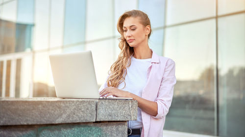 Businesswoman using laptop on retaining wall against building