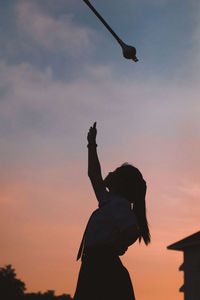 Side view of silhouette woman throwing pole against sky at sunset