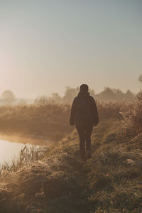 Rear view of silhouette man standing by lake against sky at sunrise