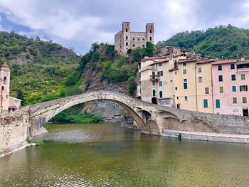 Arch bridge over river amidst buildings against sky