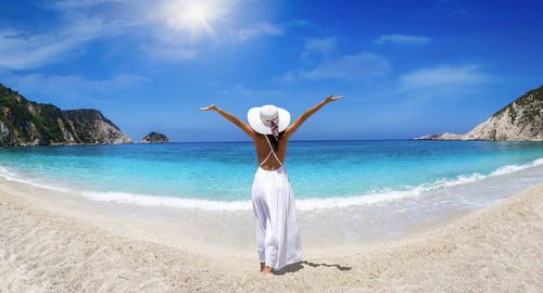 Full length rear view of woman standing at beach against sky