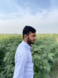 Side view of young man standing on field against sky