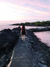 Rear view of woman walking on rock amidst sea