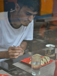 View of a young guy eating fast food in the cafe seen through the window glass. 