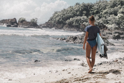 Rear view of woman holding surfboard at beach