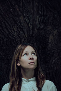 Thoughtful mid adult woman standing against tree trunk in forest