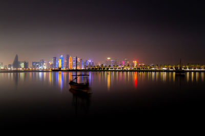 Illuminated skyline of doha, qatar at night with traditional wooden boat called dhow against sky